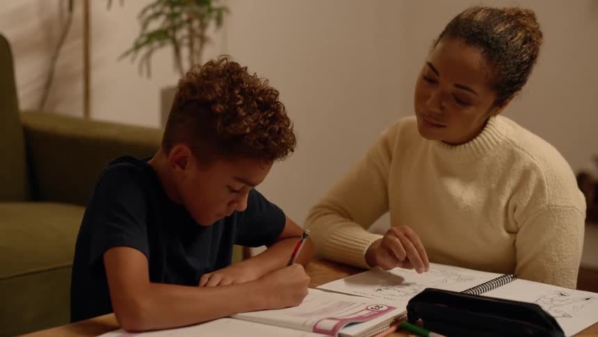 Mother sitting next to her son helping with a school assignment