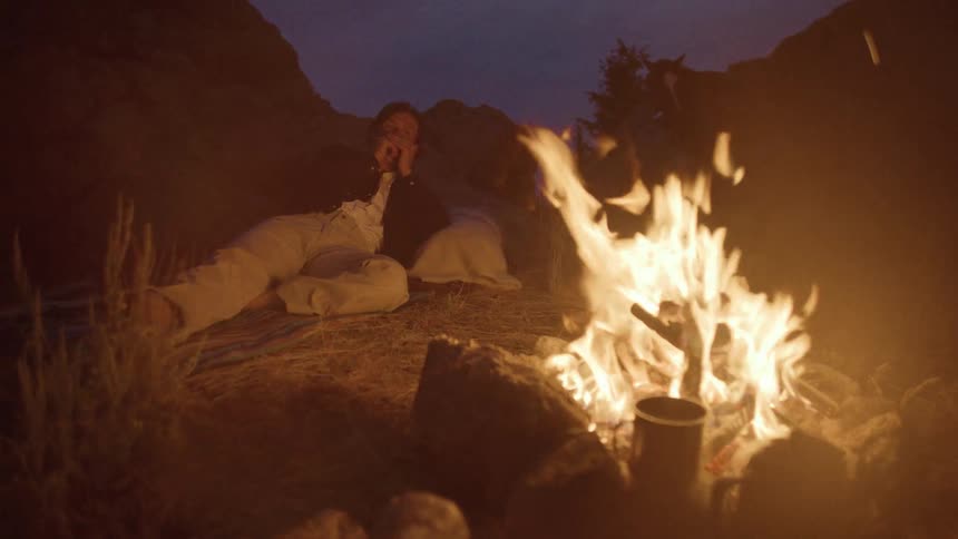 A person sitting by a campfire at dusk or night