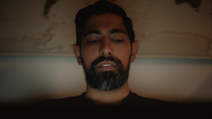 Man shaking his head while typing on a laptop at night