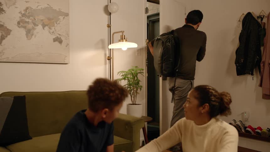 A mother and son do homework while the father enters the room