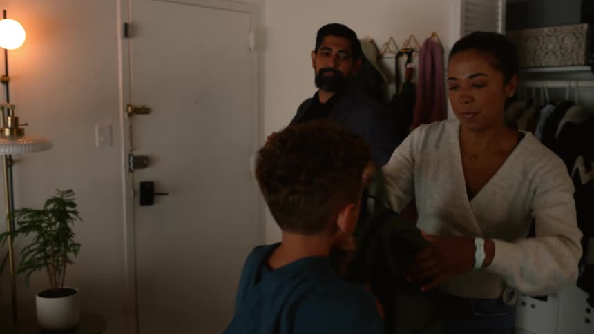 A mother and father help their son pack his backpack on the way out of their home