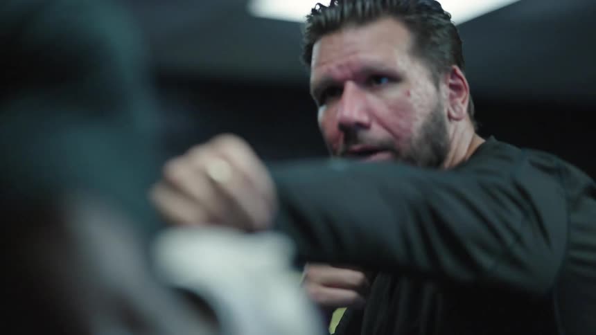 A bearded man with a focused expression extending his hand forward giving instructions in a training environment