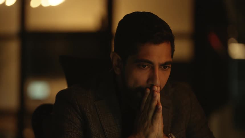 Bearded man wearing a brown blazer yawns while working on laptop at night