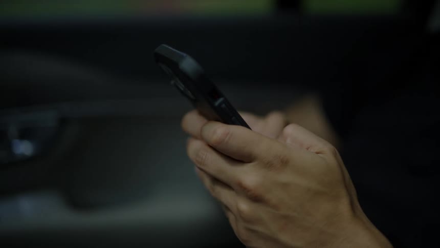 A pair of hands typing on a smartphone while traveling by car