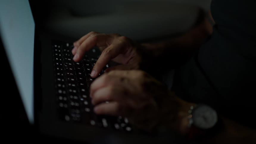Hands of a man typing on a laptop while riding in a moving car