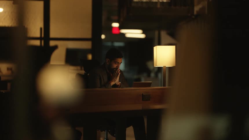 A man working on a laptop at a table in a dimly lit room with warm lighting