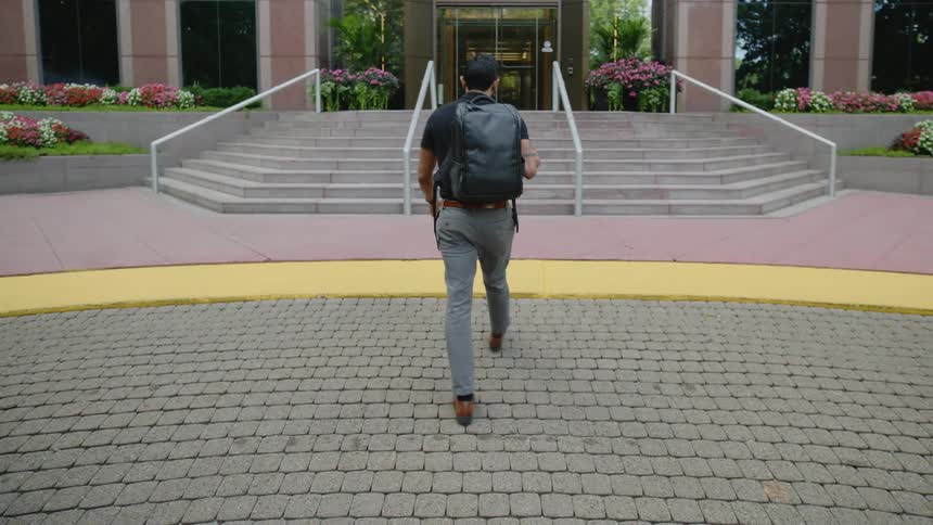 Man getting out of car slings a backpack on his shoulder and enters an office building