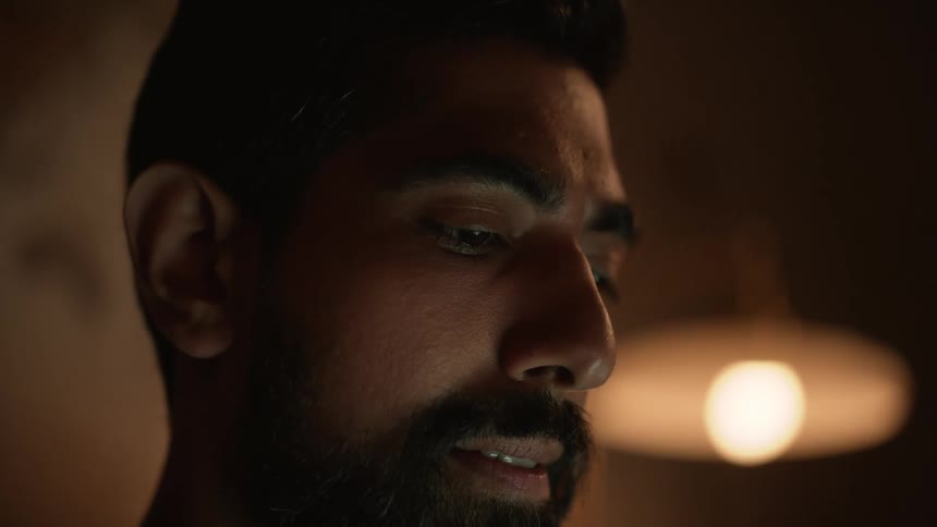 Bearded mans face looking down at laptop at night