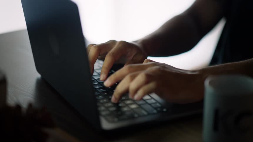 Hands of a person typing on a laptop with a coffee mug nearby
