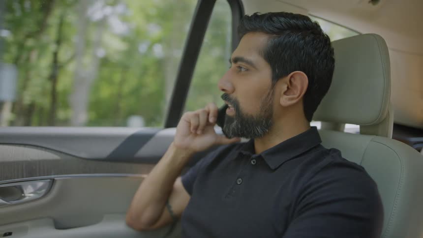 A bearded man talking on the phone while riding in a car