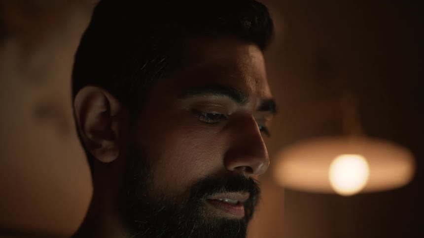 Portrait of a bearded man concentrating in a dark room with a lamp on in the background