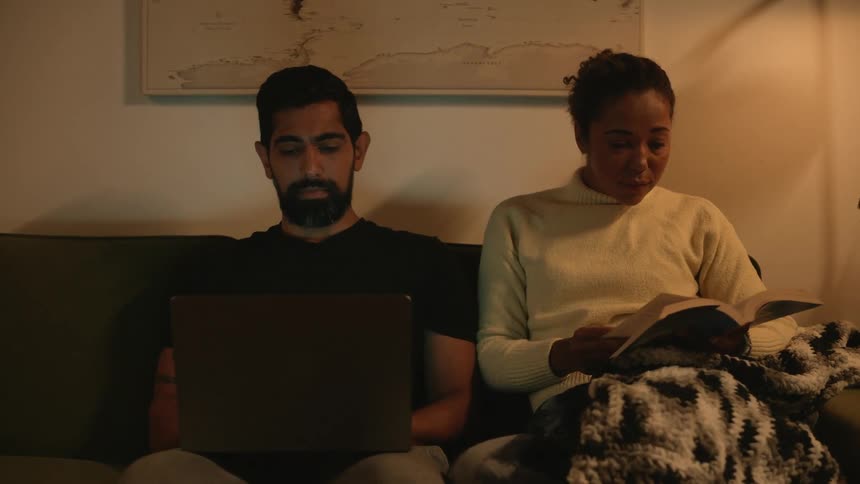 Man typing on laptop next to a woman reading a book in the living room