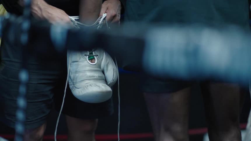 A coach helps a boxer put his boxing gloves on in order to practice