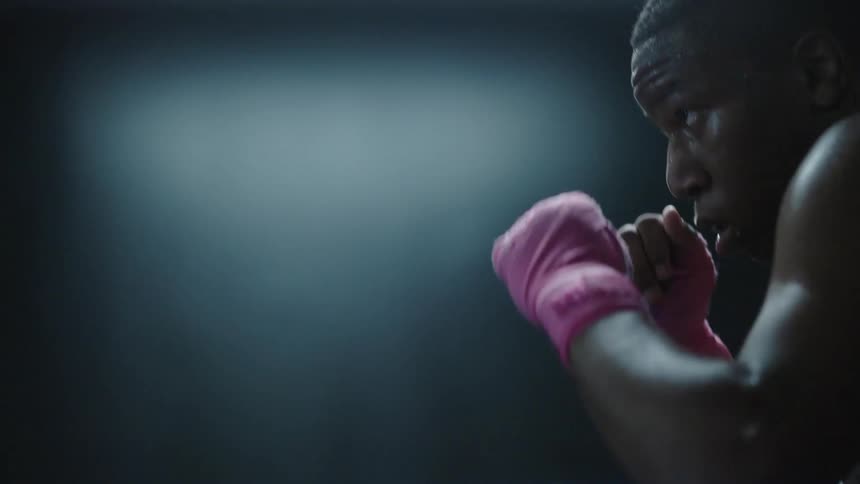 A shirtless boxer practices his punches while moving around a boxing ring