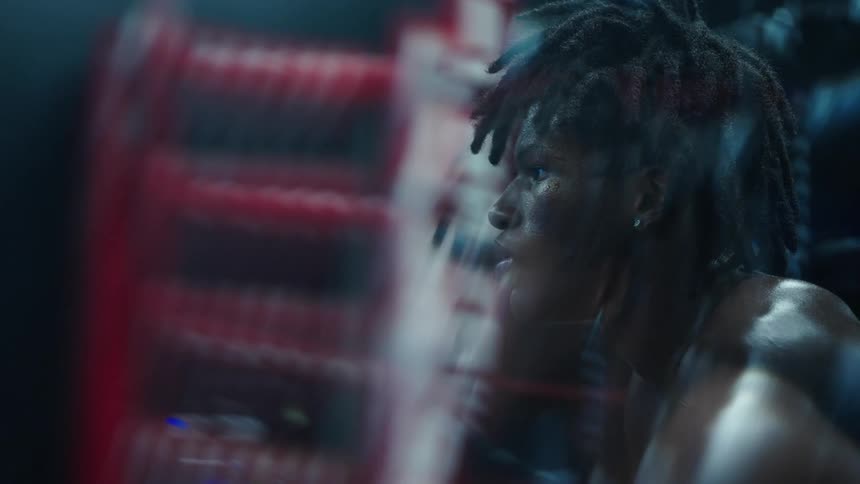 A black male with dreadlocks sits and thinks as a video game play in the background