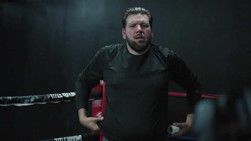Male trainer smiles briefly while watching two boxers spar in the ring during training