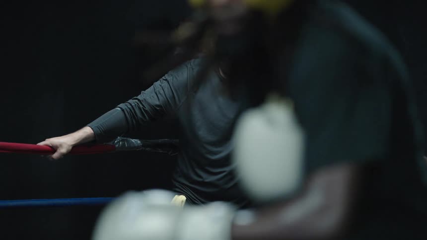 A trainer watches two men box in a ring and wipes his face with a towel