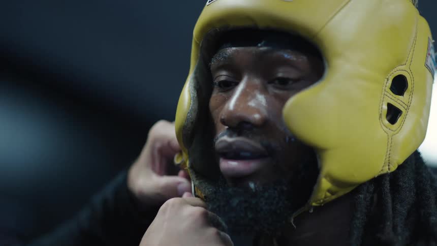 Coach rubs the boxers face gives him water and secures his headgear before the fight