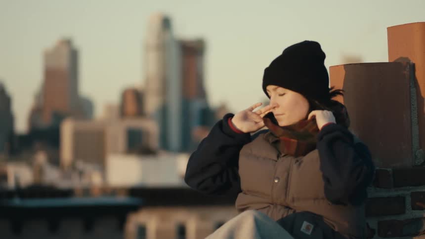 A woman adjusts her hat with a city in the background
