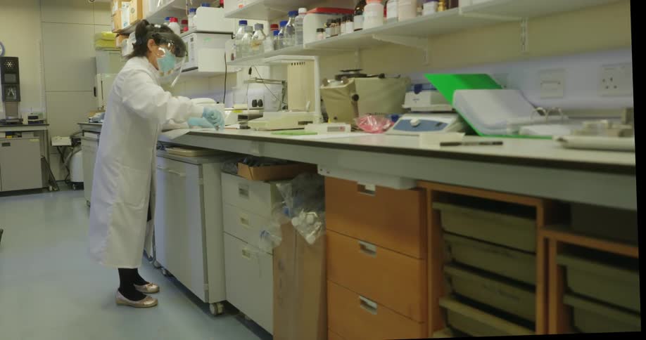 Woman in white lab coat works in a laboratory surrounded by various equipment and supplies