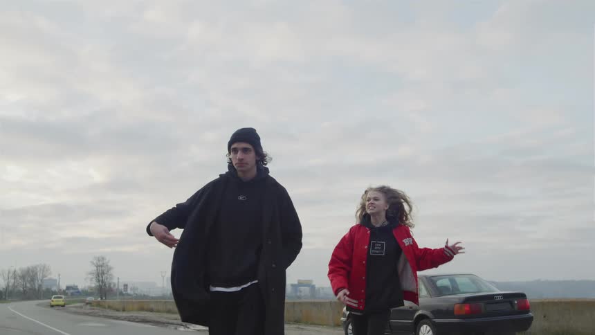 A man walks away from a car as a woman follows him and yells