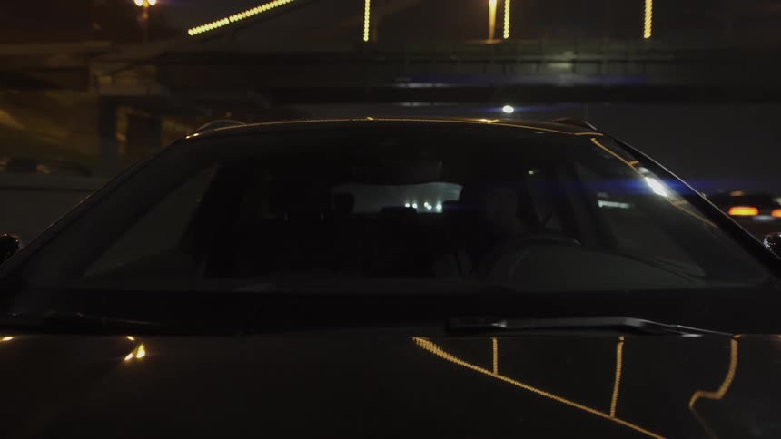 A car driving at night with reflections of surrounding lights on its surface
