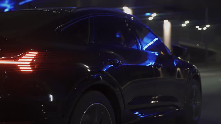 Side view of a black sedan car moving along the road at night