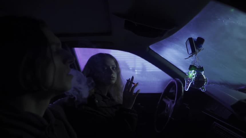 Two young people inside the car smoking cigarette
