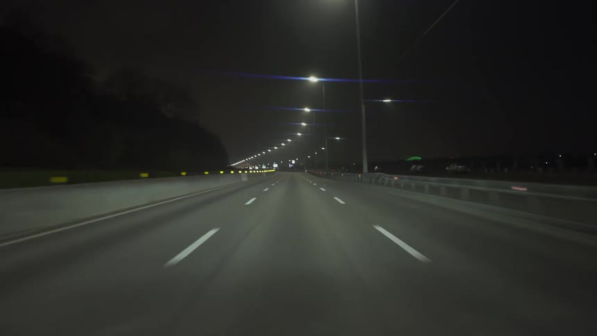 A vehicle drives down an empty highway at night