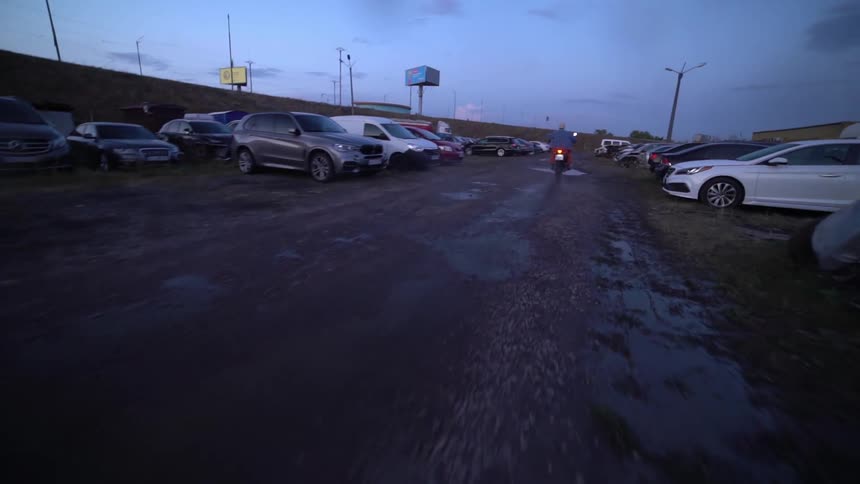 A person rides a motorcycle through a waterlogged parking lot during twilight hours