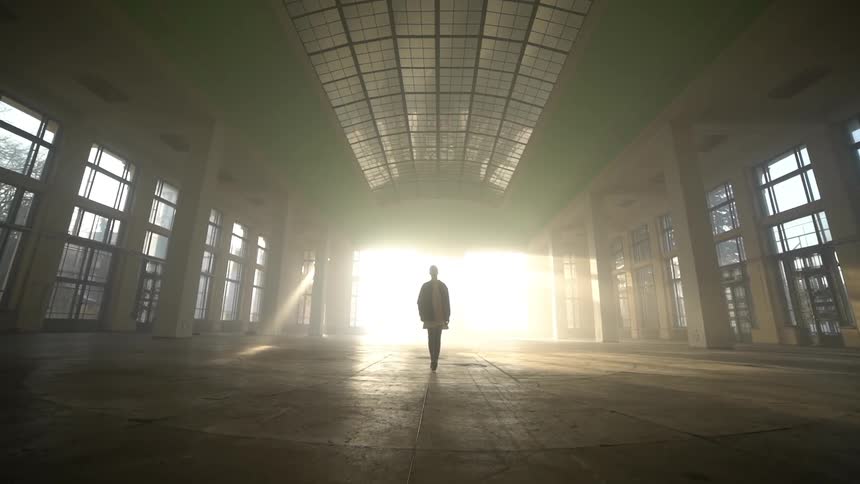 Person alone in a hall walking with sunlight in the background
