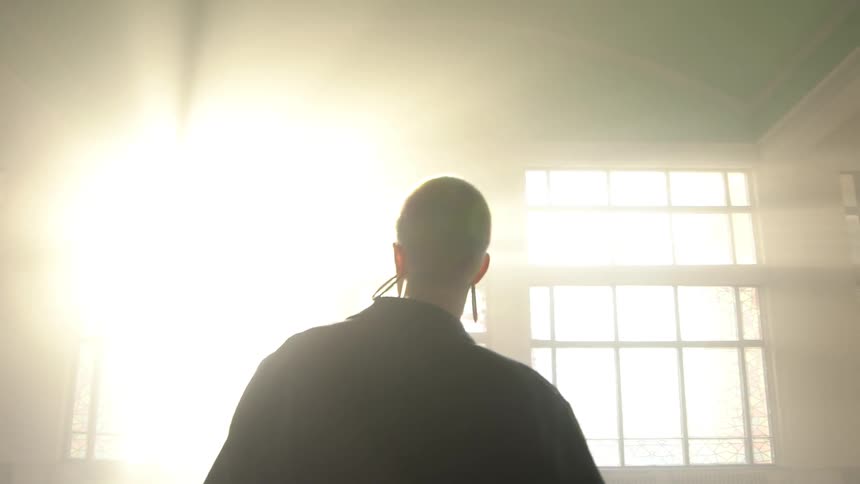 A teenage girl inside an empty building stares at the bright sunlight streaming through a large window
