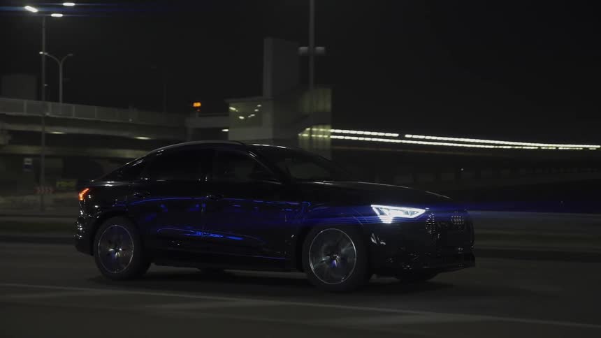 Blue car driving past a bridge at night