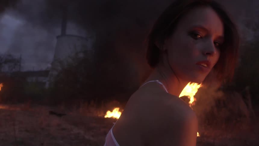 A young woman outdoors turning her head near a large fire