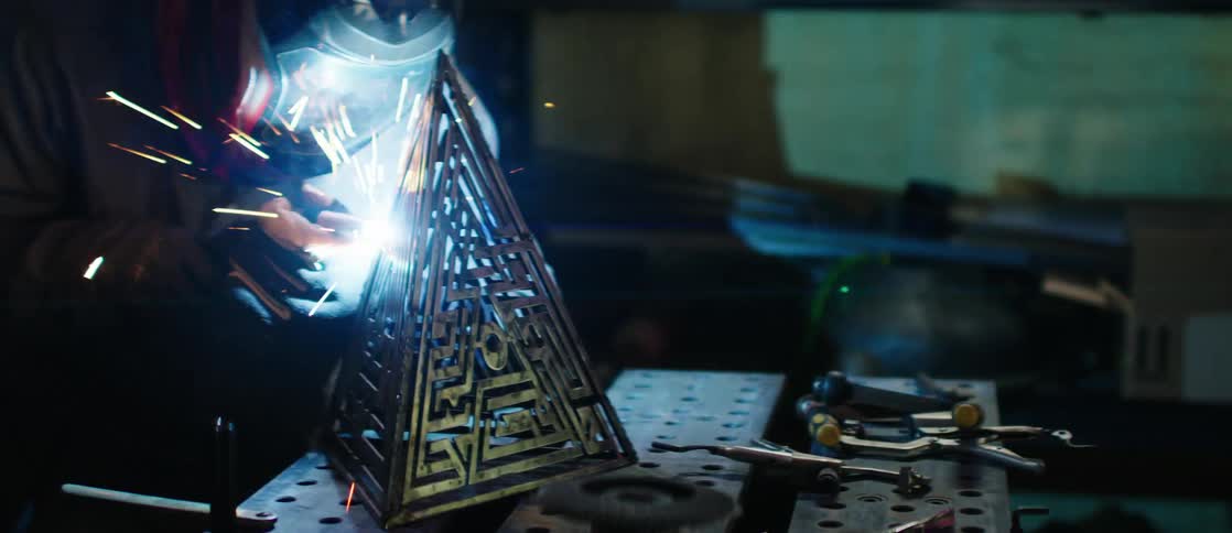 A person welding a metal structure that resembles a pyramid