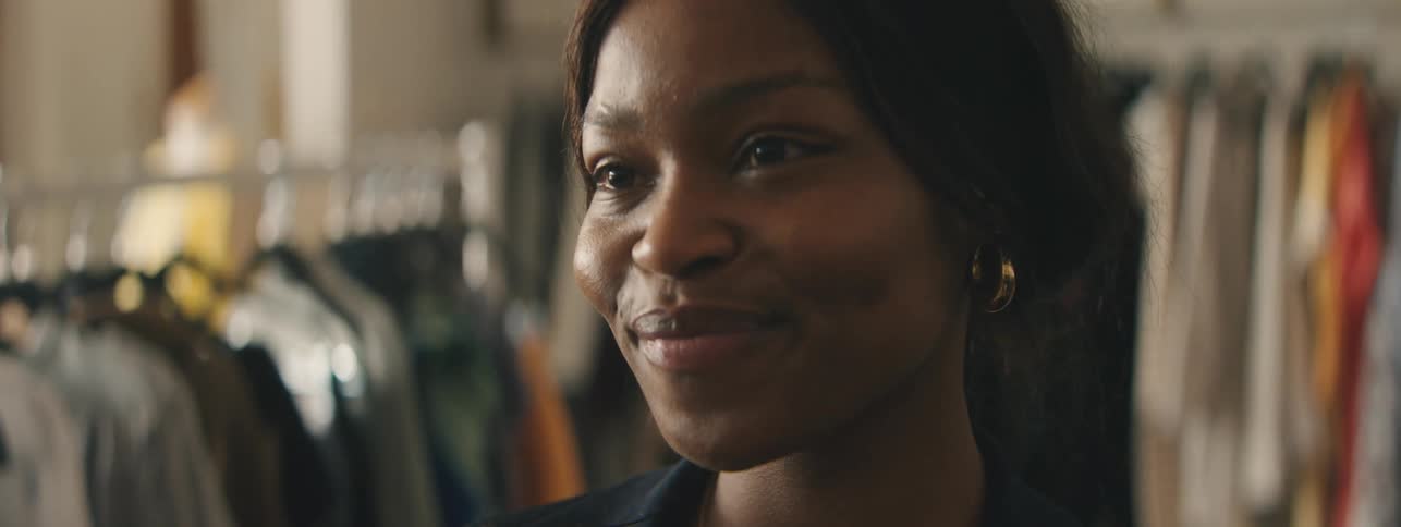 Confident Black woman posing among fashion garments in a boutique.