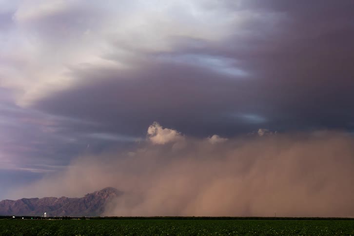 A huge sandstorm covering a mountain and a highway with some cars passing by