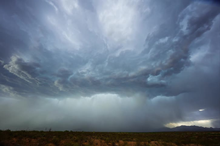 Dark turbulent storm clouds with rain hover over a mountain range