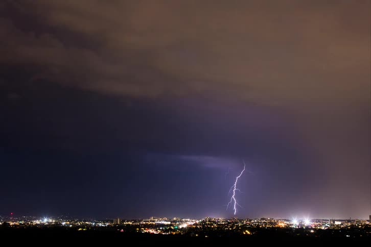Lightning strikes the night sky over an illuminated city
