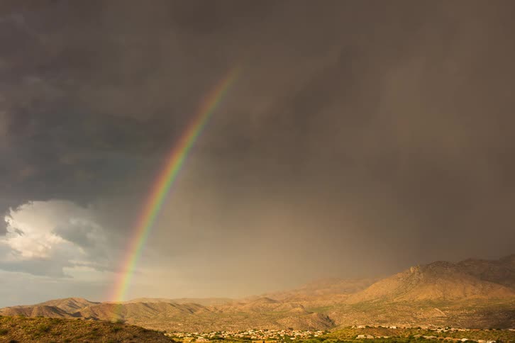Rainbow descends towards a mountainous region under stormy weather conditions