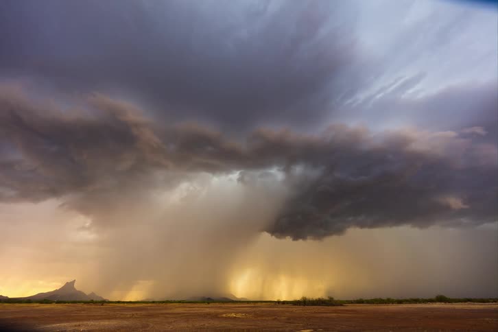 Large dark storm cloud dominates the sky casting shadows and rain over the land below