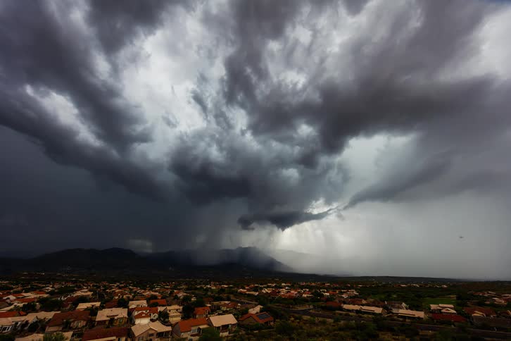Dark storm clouds dump heavy rain over an area with several homes