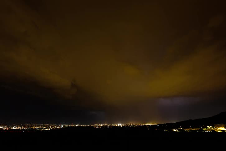 Purple lightning streaks across the night sky over an illuminated city