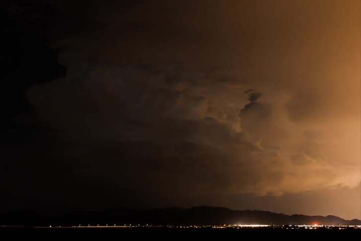 Lightning strikes the sky illuminating the clouds and the silhouette of a mountain range in the background