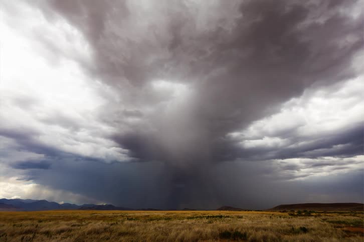 Dark clouds gather over a vast open field with a thunderstorm brewing