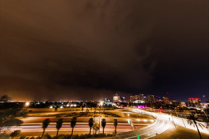 The city lit up at night contrasts with the dark cloudy sky