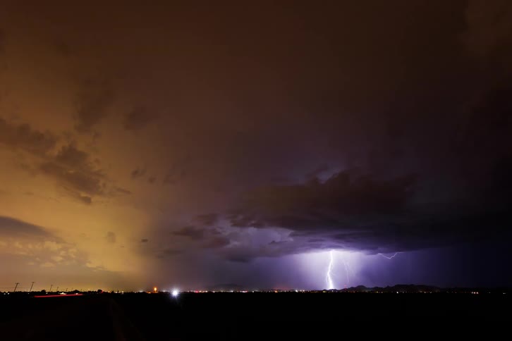 A bright lightning storm coming out of the sky one night over a highway with some cars passing by