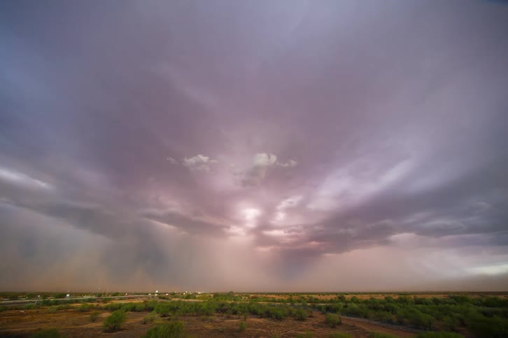 Dark storm clouds with thunder hover over a rural landscape with cars passing in the background