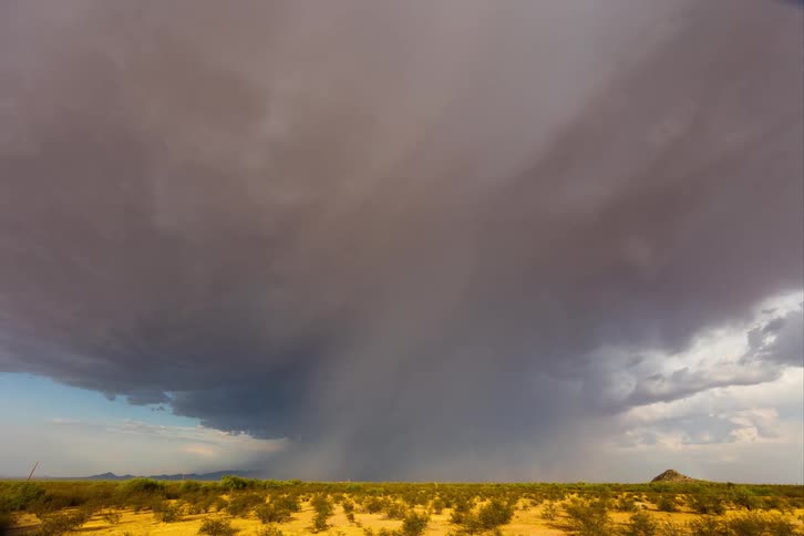 A big huge gray cloud turning into a tornado in a desert
