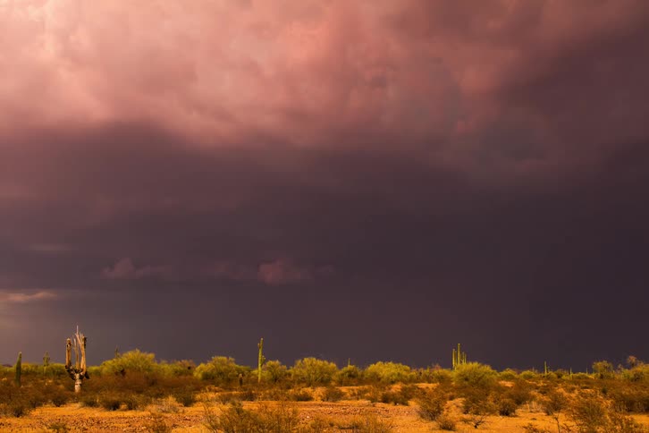 Dark storm clouds rotate and emit lightening over a desert